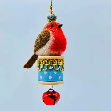 A needle felt robin with a bright red chest and a gold and blue crown, sitting atop a gold and blue bobbin with a red bell hanging from the bottom