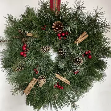 A natural Christmas wreath made of pine, with red berries, cinnamon sticks and brown pine cones for decoration