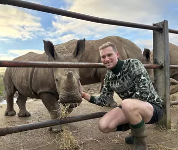 Keeper Alex wearing a Christmas jumper posing next to rhino calf Benja