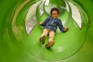 A little boy going down a green tube slide