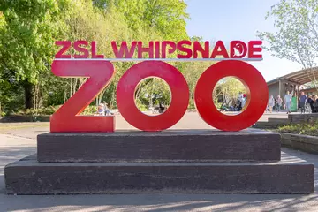 The red Whipsnade Zoo sign with trees in the background