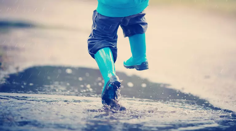 A child wearing blue wellies jumping in a puddle