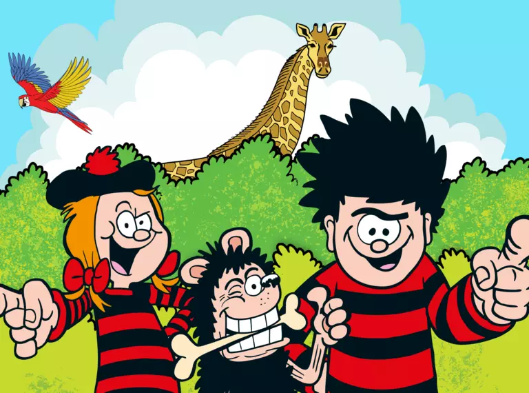 Dennis Menace, Gnasher and Minnie are pointing and displaying thumbs up to the viewer in the foreground, while in the background is a double hedge line in shades of green, a giraffe and a parrot in front of a blue sky background