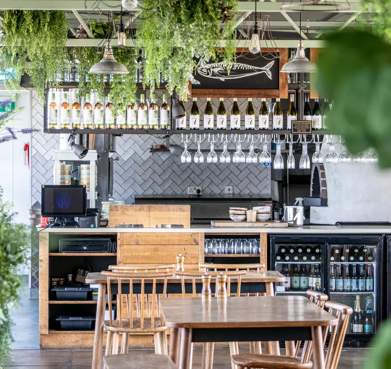 The inside decor of Viewpoint restaurant at Whipsnade Zoo, showing tables with chairs, fridges full of drinks, and green foliage